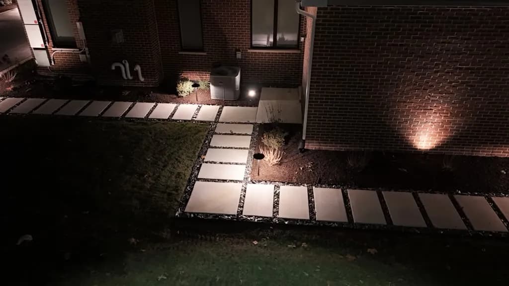 Large-format square paver walkway with dark cobble borders at night and landscape uplighting on a brick house wall in Chicago's Southwest Suburbs