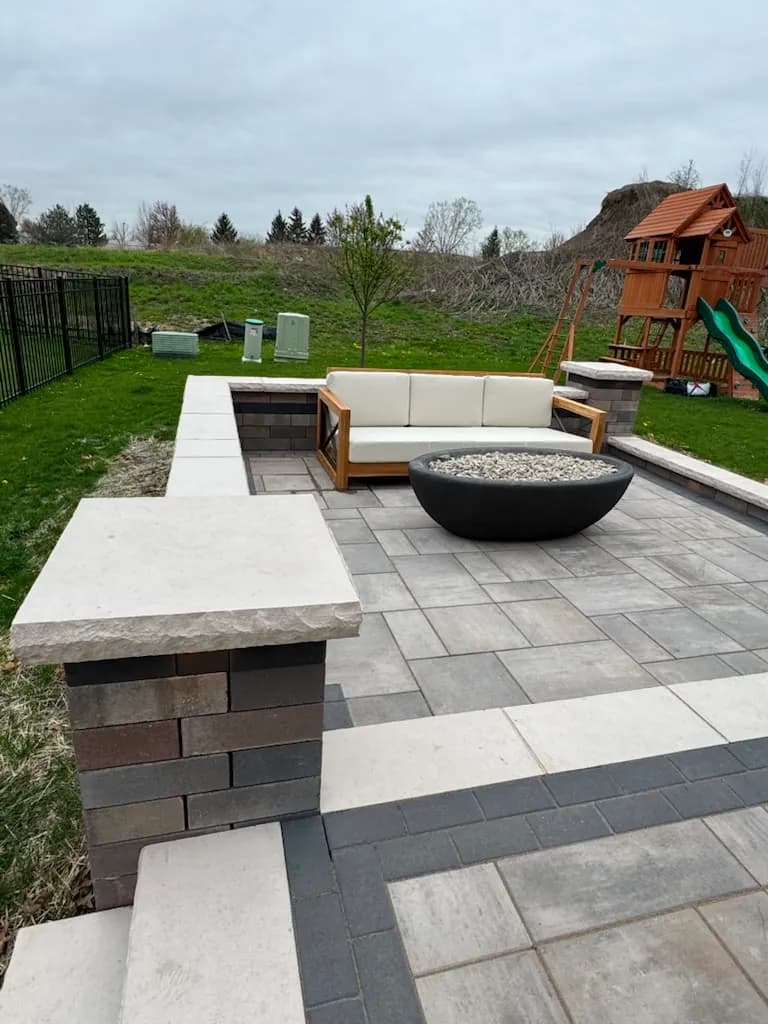 Multi-tone paver patio with seat walls, capped columns, teak seating, and a modern black fire bowl in Chicago's Southwest Suburbs