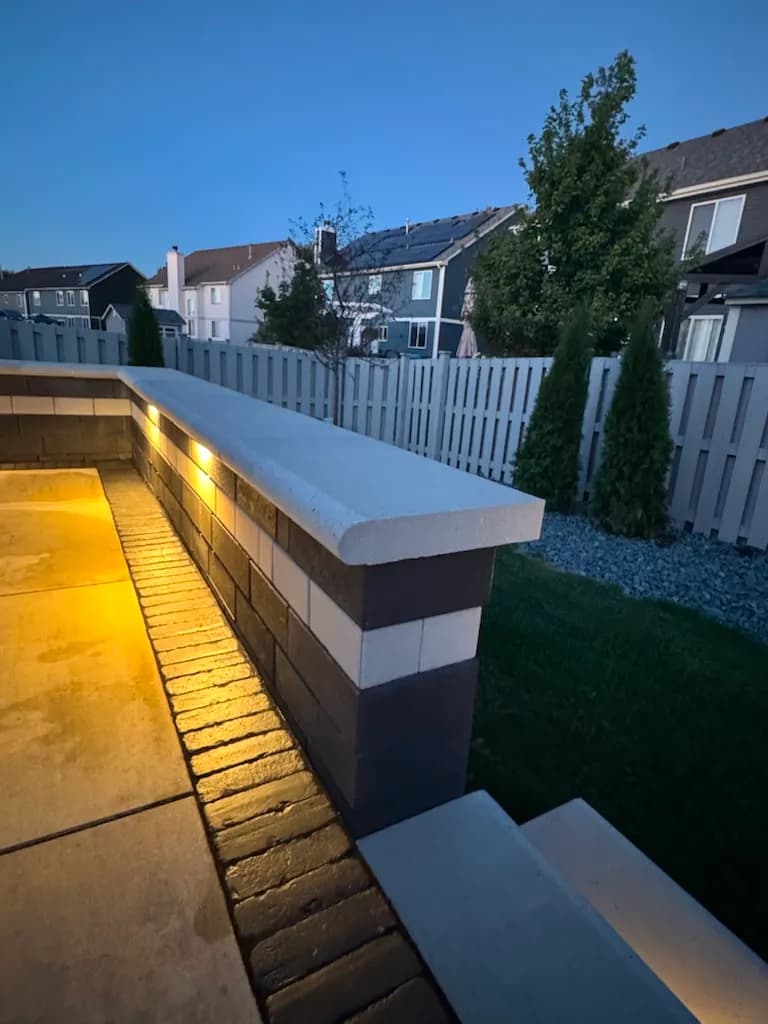 Long two-tone block seat wall with smooth cap stone and warm under-cap LED lighting at dusk beside a concrete patio in Chicago's Southwest Suburbs