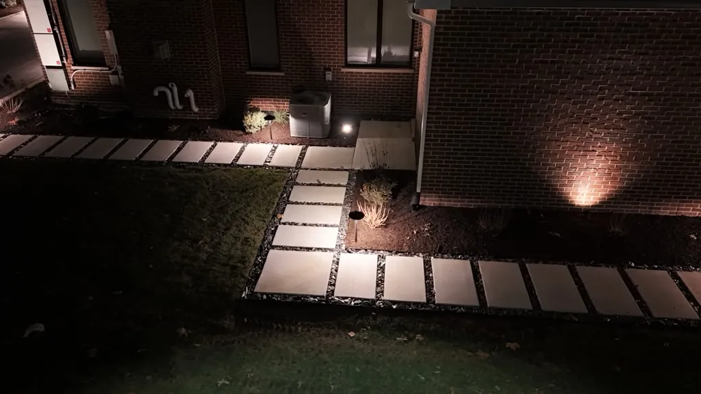 Large-format square paver walkway with dark cobble borders at night and landscape uplighting on a brick house wall in Chicago's Southwest Suburbs
