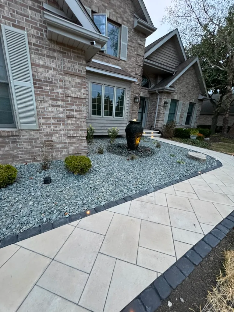 Light large-format paver front walkway with a dark cobble border, decorative gray stone bed, black urn bubbler fountain, and landscape lighting in Chicago's Southwest Suburbs